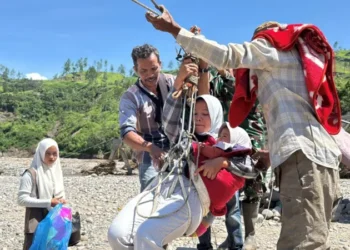 Khairunnisa bersama bayinya berusia 1,5 tahun tak punya pilihan untuk berobat dan mencari kebutuhan hariannya menggunakan jembatan darurat. Ia menggunakan sling baja ini "tidak terhitung" tapi tetap khawatir dengan risiko terjatuh dan terhanyut di sungai deras. (foto : bbc)