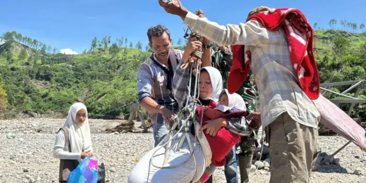 Khairunnisa bersama bayinya berusia 1,5 tahun tak punya pilihan untuk berobat dan mencari kebutuhan hariannya menggunakan jembatan darurat. Ia menggunakan sling baja ini "tidak terhitung" tapi tetap khawatir dengan risiko terjatuh dan terhanyut di sungai deras. (foto : bbc)